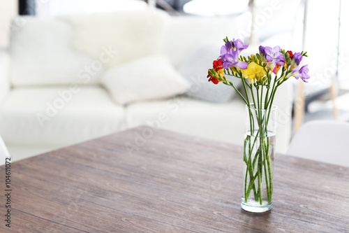 Beautiful bouquet of colorful freesias flowers on wooden table at living room