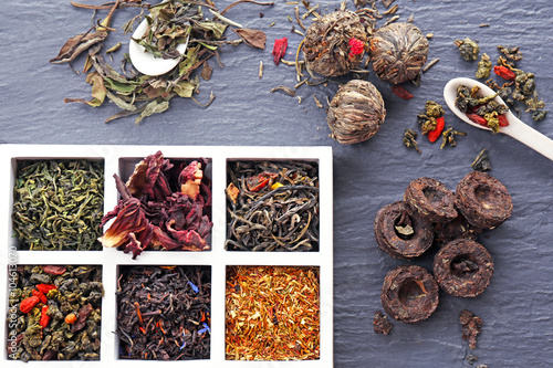 Variety of dry tea in wooden box with spoons on grey background photo