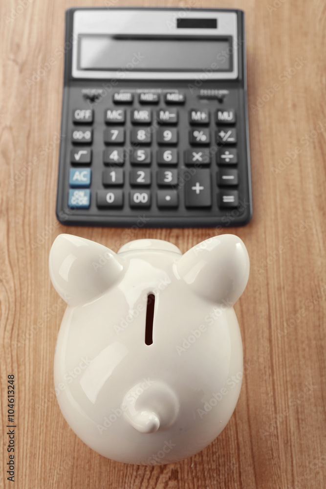 White piggy bank with calculator on wooden background White piggy bank with calculator on wooden background