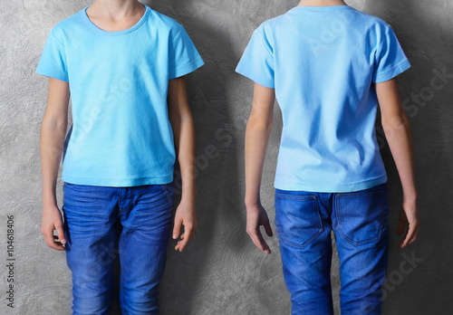 Clothes advertising. Boy in blue T-shirt and jeans on grey wall background