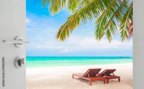 Fototapeta Naklejka Na Ścianę i Meble -  opened white door to beautiful beach with beach chairs under coconut tree