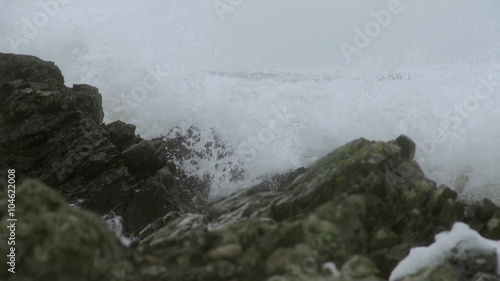 Storm Waves Crashing On Large Rocks As The Waves Hit Shore. Slow motion footage of large storm waves crashing on rocky cliffs. photo