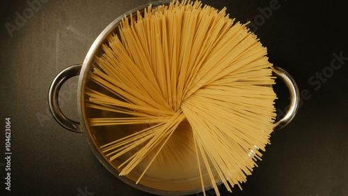 TOP VIEW: A cook puts down a spaghetti in a steel pot (round)
