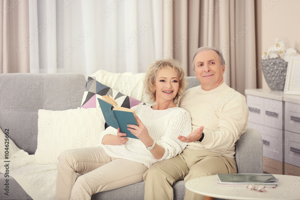 Mature couple reading book together on a sofa at home