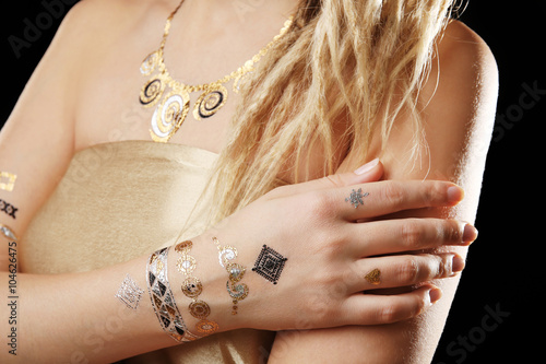 Young blonde girl with golden and silver flash tattoo on black background © Africa Studio