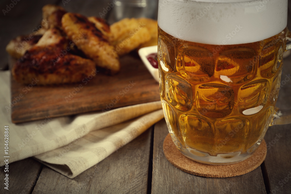 Glass of beer and chicken wings on wooden table, close up Glass of beer and chicken wings on wooden table, close up