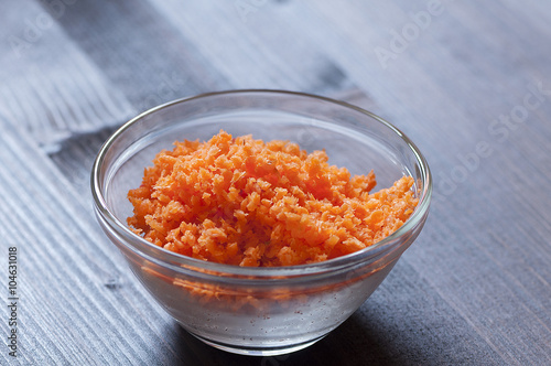 Minced carrots in a glass bowl on a wood background