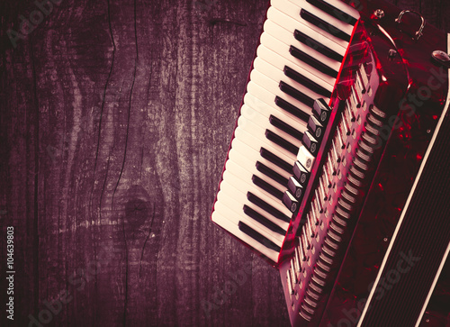 Part red accordion on wooden grey background. Write text. Vintage