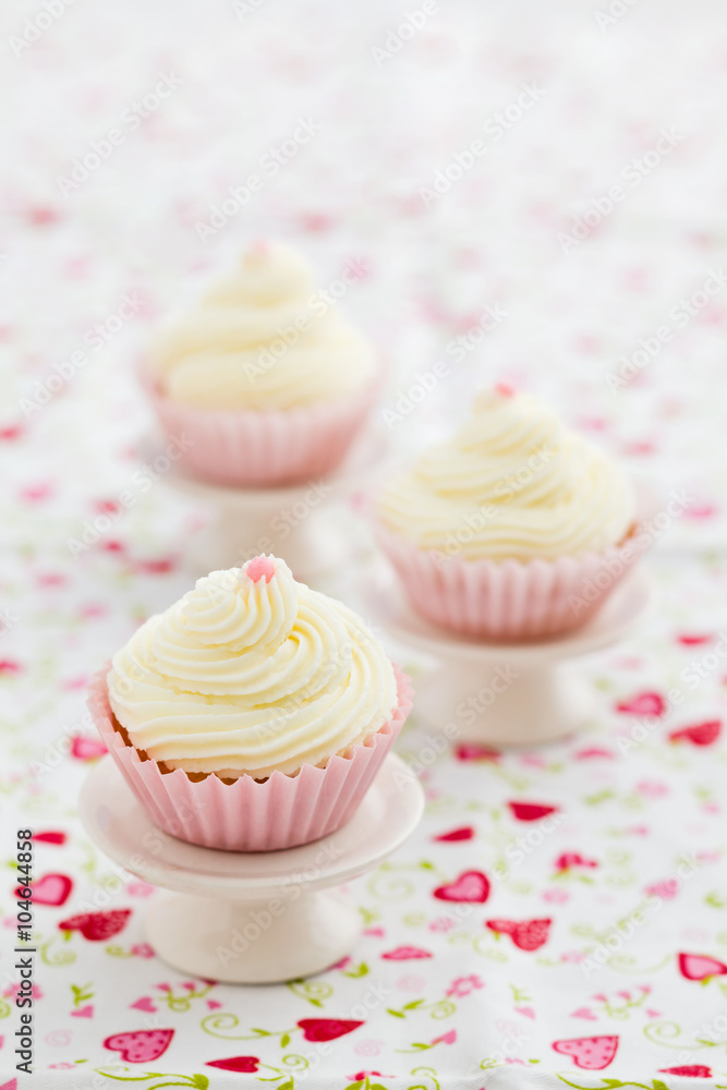 Three vanilla cupcakes with buttercream swirl topping on mini cake stands Three vanilla cupcakes with buttercream swirl topping on mini cake stands