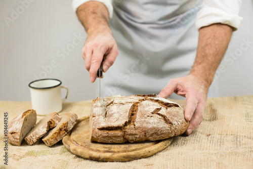 Male cook cuts bread. Rustic style.