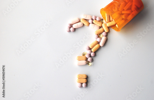 different drugs and health supplement pills in a question mark poured from a medicine bottle photo