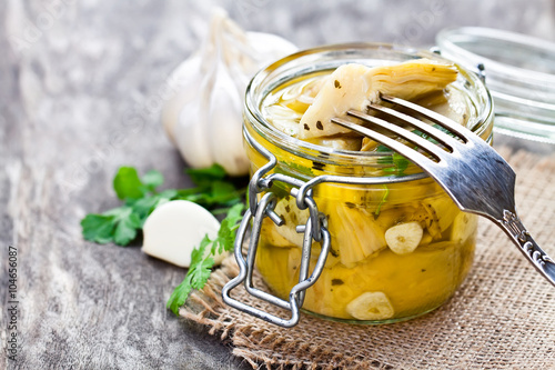 Pickled  artichoke with garlic in a glass jar on rustic wooden t