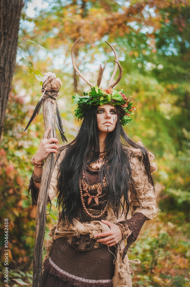 beautiful brunette with painted face, in a flower wreath and a wooden staff in his hand, looking forward belligerently beautiful brunette with painted face, in a flower wreath and a wooden staff in his hand, looking forward belligerently
