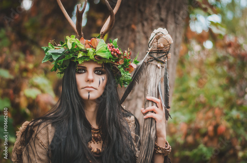 portrait of a beautiful brunette in the form of shaman, with floral wreath on her head and horns