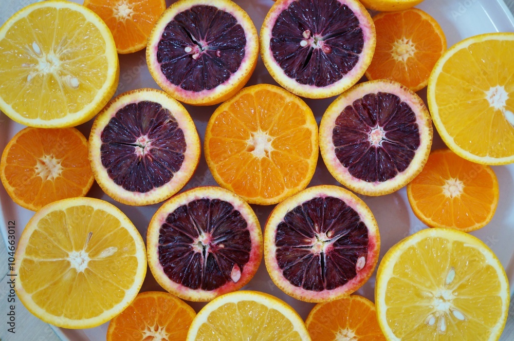  Ruby red blood oranges, navel oranges, and clementines cut in half on a white platter 

