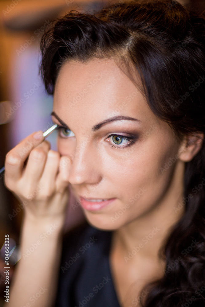 Make-up artist applying bright base color eyeshadow on model's eye and holding a shell with eyeshadow on background, close up Make-up artist applying bright base color eyeshadow on model's eye and holding a shell with eyeshadow on background, close up