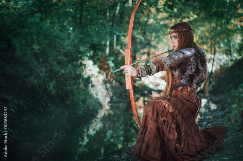 Foto Woman hunter with a bow in hand, taking aim at his prey in the forest