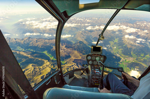 Fotografie Helicopter cockpit flying on mountain landscape and cloudy sky, with pilot arm driving in cabin