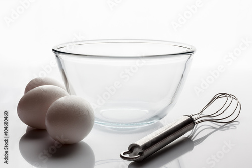 Glass transparent bowl with metal whisker and three white eggs aside from side
