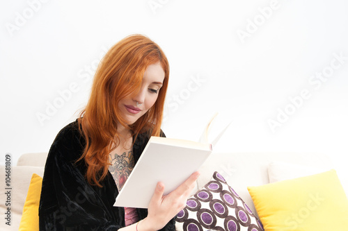 Young redhead woman smiling and reading a book