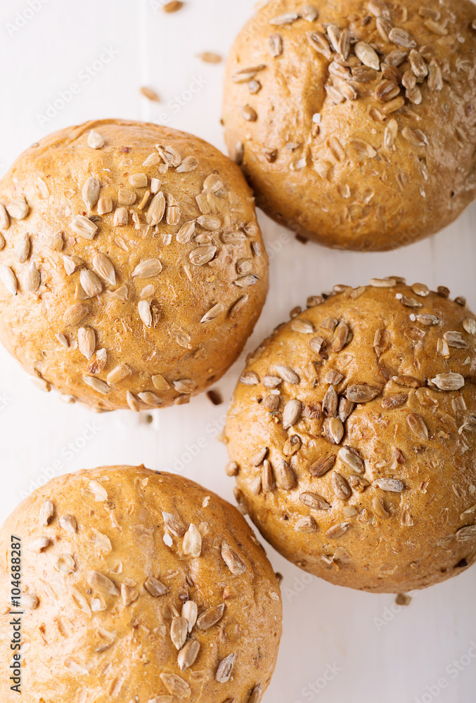 Four buns with seeds on a light wooden background, top view 