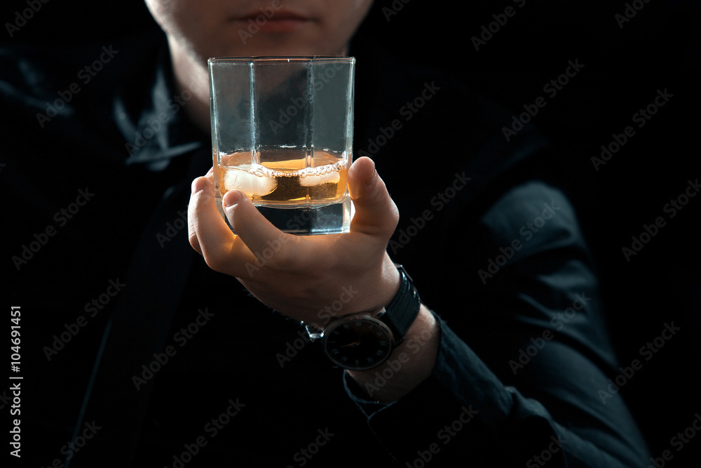 Closeup man in black with glass of whiskey and ice in dark room Closeup man in black with glass of whiskey and ice in dark room