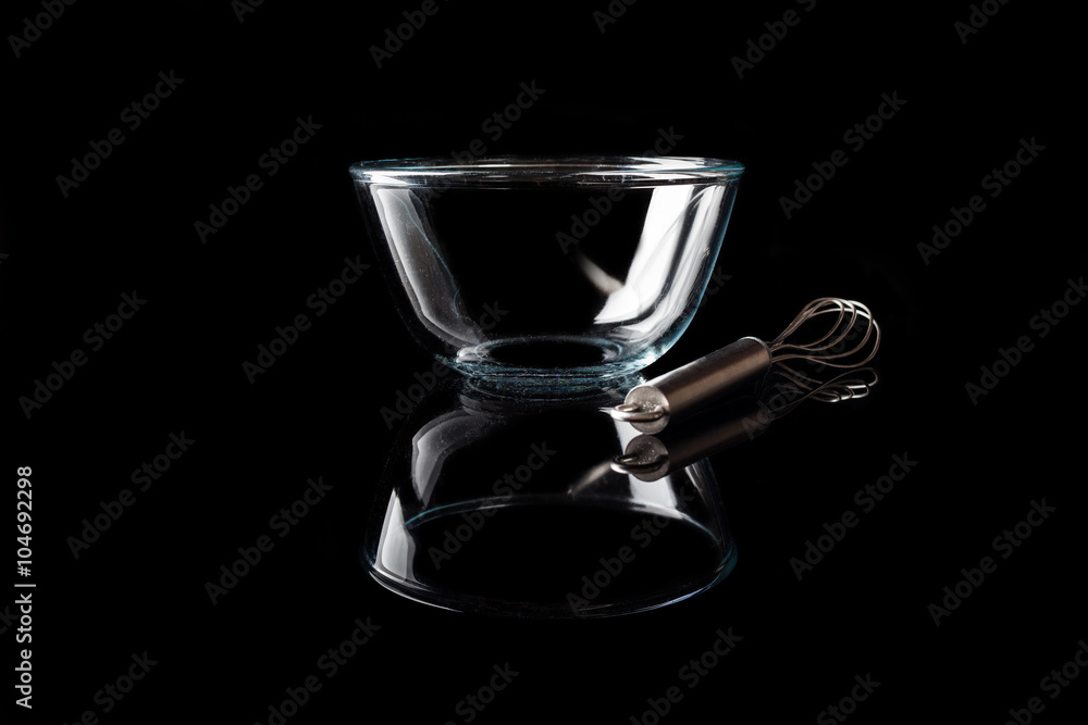 Glass transparent bowl with metal whisker aside on black background side view with reflection Glass transparent bowl with metal whisker aside on black background side view with reflection
