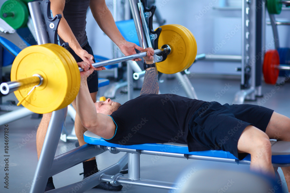 Fototapeta premium Young man lifting the barbell in gym with instructor