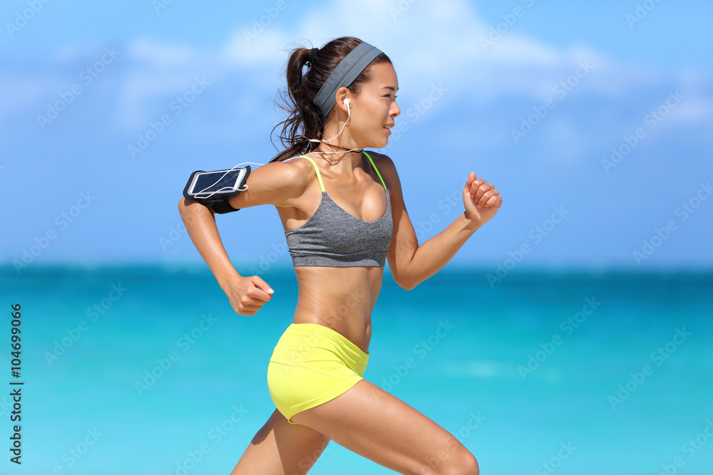 Athlete running woman runner listening to music on her phone sports armband  with touchscreen and headphones earphones on summer beach. Fitness girl  jogging fast training cardio and glutes. Stock Photo