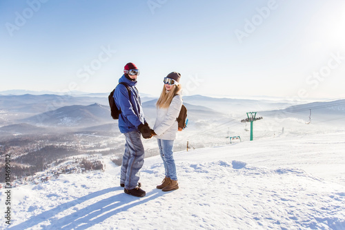 Girl and guy in masks for snowboarders holding hands on the background of the ski slopes