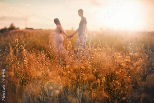 Blurred silhouettes of a boy and a girl at sunset reaching the ears in the foreground