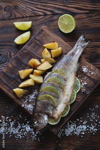 Baked trout fish with lime and potato in a rustic wooden setting