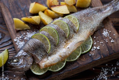 Close-up of a rainbow trout baked with lime and potato wedges
