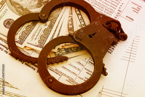 many dollar bills with handcuffs, on tax form background