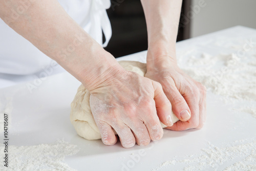 Woman's hands knead dough on a table