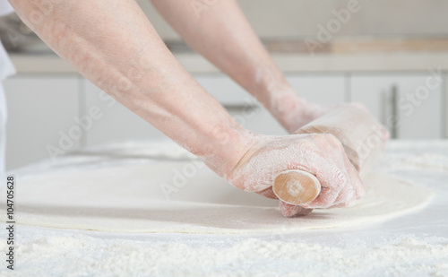 Housewife flattening a dough with a rolling pin