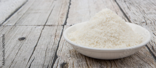 Dried coconut powder in white bowl over wooden background