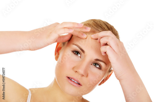 Unhappy young woman squeezing pimple on face