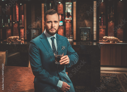 Confident well-dressed man with glass of whisky in luxury apartm photo
