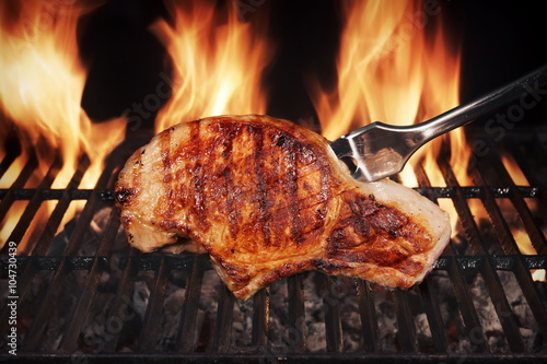 Pork Steak On Hot Flaming Barbecue Grill With Fork