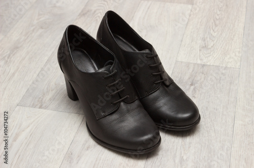 Female black leather shoes on high hill, wooden background