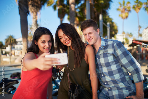 friends taking selfies under the shade of palm trees at santa monica beach
