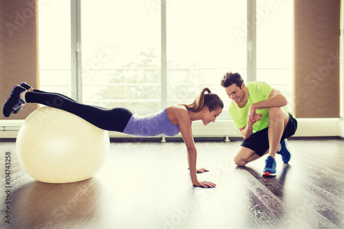 smiling man and woman with exercise ball in gym