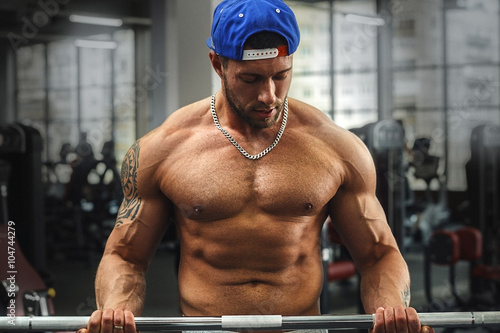 Young muscular man doing exercise with barbell in the fitness gym