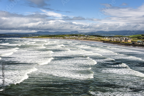 Irland, Rossnowlagh: Panorama Blick auf wunderschöne wilde irische Küste mit Wellen Ozean Meer Stadt Horizont Wolken und blauem Himmel 