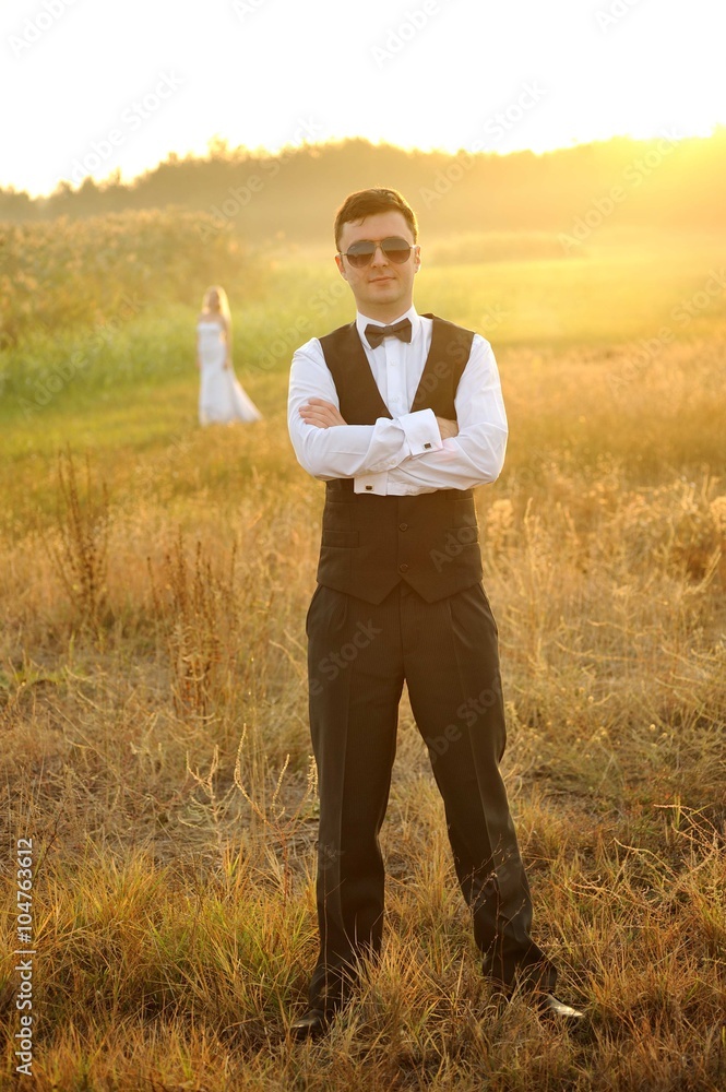 Groom In a vested suit posing in the field Groom In a vested suit posing in the field
