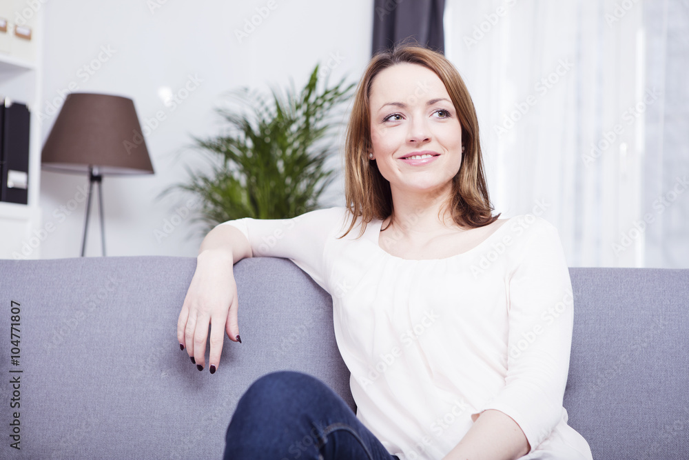 Happy smiling brownd haired young woman sitting on a couch having her arm on the backrest Happy smiling brownd haired young woman sitting on a couch having her arm on the backrest