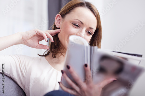 Beautiful young brown haired girl reading a magazine while sitting relaxing on a couch