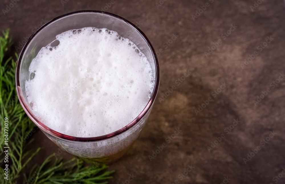 Glass full of beer and green branch on light brown background Glass full of beer and green branch on light brown background