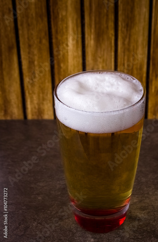 Glass full of beer on flat base and wooden background 